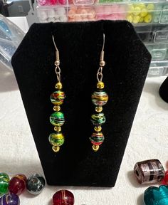 Green and gold  glazed bead earrings with wire hook assembly with gold resin dividers. Glazed in mainly green and gold but with a touch of red and black glaze. Perfect for any occasions. One of a kind Gold Earrings With Colorful Beads For Party, Green Gold Beaded Drop Earrings, Green Drop Earrings With Gold Beads, Green Beaded Earrings For Festive Occasions, Festive Green Beaded Drop Earrings, Green Beaded Drop Earrings For Festive Occasions, Multicolor Drop Earrings With Gold Beads, Unique Green Earrings With Colorful Beads, Festive Green Earrings With Colorful Beads