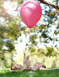 two children laying in the grass with a pink balloon