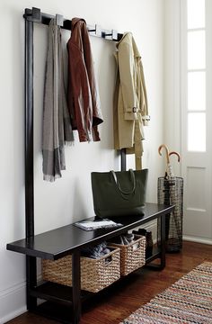 a coat rack with two coats hanging on it next to a bench and baskets filled with purses