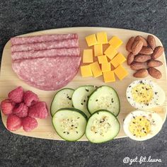 a wooden cutting board topped with meat, cheese and veggies next to nuts