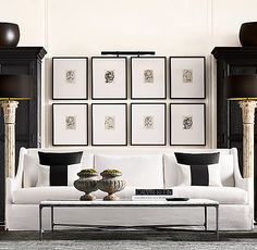 a living room filled with white furniture and framed pictures on the wall above it's coffee table