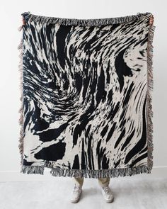 a woman standing in front of a black and white blanket with fringes on it