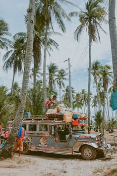 people standing on the beach next to a truck with luggage strapped to it and palm trees in the background