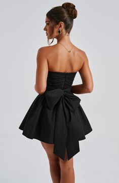 THE dress of the season has landed and you're going to be obsessed. Meet Katrina, our dreamy mini with a pretty, voluminous skirt and waist cinching bodice. Fastening with a zip to the back, tie with an oversized bow to complete the look for perfect feminine drama. 



Colour: Black.

Premium non-stretch cotton blend fabric.

Fully lined.

Strapless ruched bodice with boning.

Waist cinching.

Oversized tie to create bow detail to back.

Voluminous skirt with tulle lining.

Zip fastening to the reverse.

Mini length.

 Size: XS, S, M, L, XL, XXL Cocktail Dress With Gathered Voluminous Skirt, Cocktail Dress With Voluminous Gathered Skirt, Evening Dresses With Ruched Voluminous Skirt, Mini Corset Dress With Pleated Bodice For Night Out, Prom Mini Dress With Pleated Bodice, Ruched Mini Corset Dress For Cocktail, Cocktail Mini Corset Dress With Ruched Detail, Pleated Bodice Mini Dress For Prom, Prom Dress With Pleated Waist And Fitted Bodice