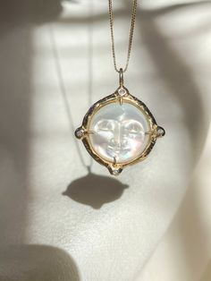 A dreamy 15mm hand-carved Mother of Pearl Moon encircled in gold, set with (4) White Diamonds, set on a solid 14k yellow gold 0.8mm box chain. (Approx. 5.7g.) Inspired in essence by the Impressionist French composer Claude Debussy, Clair de Lune translates to pale blue light or moonlight, and embodies the Divine Feminine energy of the moon, wholly encapsulating the deep sense of serenity found through inner self-awareness, and the strength kept within the gentleness of the heart. Aligns with int Elegant Oval Moon Phase Jewelry, Elegant Oval Jewelry With Moon Phase, Celestial Round Pendant Jewelry With Hallmark, Celestial 14k Gold Coin Pendant Jewelry, Celestial 14k Gold Jewelry With Coin Pendant, Medallion Jewelry With Sun And Moon Design As Gift, Elegant Sun And Moon Design Jewelry As Gift, Elegant Sun And Moon Design Jewelry Gift, Elegant Sun And Moon Design Jewelry For Gifts