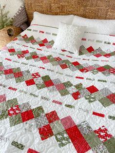 a bed with a white and red quilt on it's headboard next to a wicker basket