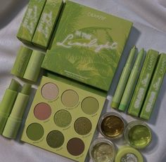 the contents of a green makeup set on a white sheeted surface, including eyeshades and eyeliners