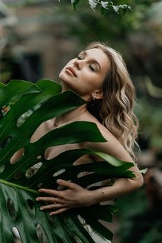 a woman with her eyes closed standing behind a large green leaf