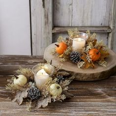 two candles are sitting on top of a wooden tray with flowers and pineconis