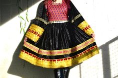 This is a richly textured traditional Afghan dress and Its main fabric is velvet, in a deep, luscious black that gives it a luxurious sheen. The dress features vibrant patterns and colors on the chest which is hand knotted and cuffs, with a geometric design that includes shades of red, orange, and green. A standout feature is the elaborate gold embroidery and trim that adorn the hem and cuffs, adding a regal touch. Traditional Black Ceremonial Dress, Black Festive Dresses With Traditional Patterns, Black Dresses With Traditional Patterns For Festive Occasions, Festive Black Dress With Traditional Patterns, Festive Black Dresses With Traditional Patterns, Traditional Festive Winter Dresses, Traditional Winter Festive Dresses, Black Traditional Drape Dress For Festivals, Black Traditional Drape Dress For Ceremonies