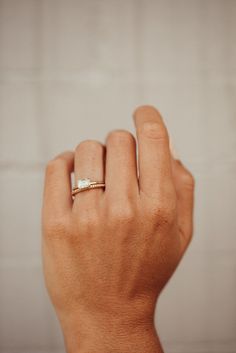 a woman's hand with a gold ring on her left wrist and a white brick wall in the background