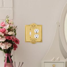 there is a vase with pink flowers next to a mirror and an electrical outlet on the wall