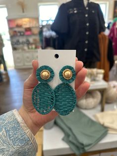 a person holding up a pair of earrings in front of a store display case with other items on it