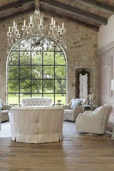 an elegant living room with white furniture and chandelier hanging from the ceiling in front of a large window