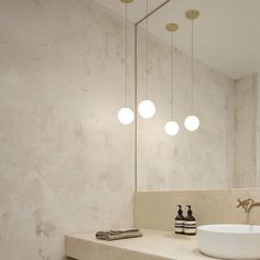 a bathroom with marble counter top and white sink under three round light fixturees hanging from the ceiling