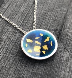 "This enamel pendant is made from Sterling Silver with enamel and fine gold detail. The cup-shaped pendant has beautiful blue and turquoise enamels and 22ct gold foil detail sealed securely. It has a flat, silver circumference and measures approx. 2cms in diameter. Inspired by an atlas this minimalist piece had a contemporary feel. The pendant hangs on an 18\" Sterling Silver chain and matching studs are also available." Yellow Gold Enamel Oval Pendant Necklaces, Gold Enamel Necklaces With Detachable Pendant, Gold Enamel Necklace With Detachable Pendant, Gold Round Necklace With Black Enamel, Enamel Necklace With Detachable Pendant, Blue Medallion Jewelry With Polished Finish, Gold Enamel Round Pendant Necklace, Blue Enamel Oval Pendant Jewelry, Blue Enamel Round Pendant Necklace