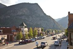 cars are parked on the street in front of buildings with mountains in the back ground