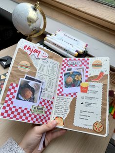 a person holding up a scrapbook with pictures on it and some crayons