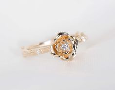 a gold ring with a flower and two small diamonds on the side, sitting on a white surface