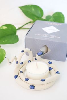 a candle sitting on top of a white table next to a box and green leaves