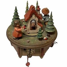 a small clock with figurines on top of it and trees around the clock