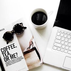 an open magazine sitting on top of a white desk next to a laptop and a cup of coffee