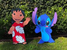 two cardboard cut outs of cartoon characters standing in the grass with bushes and shrubs behind them