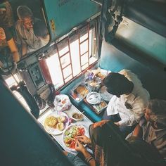 people are sitting at a table with food and drinks on it, looking out the window