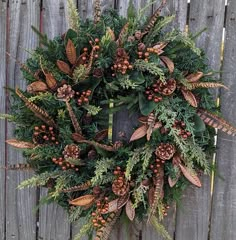 a wreath with pine cones and evergreens hanging on a wooden fence next to some plants