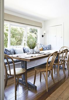 a dining room table with four chairs and a bench in front of the window,