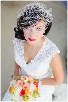 a woman in a wedding dress holding a bouquet and veil on top of her head