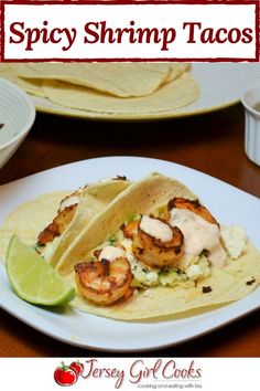 two shrimp tacos on a white plate with lime wedges next to it and the title spicy shrimp tacos