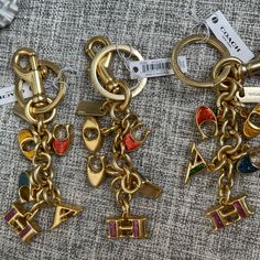 two gold colored key chains with charms attached to them on top of a piece of fabric