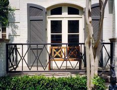 a wooden bench sitting in front of a white brick building with shutters on each side