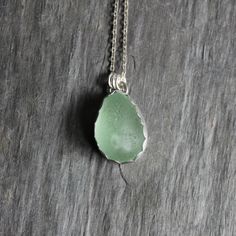 a green sea glass pendant on a silver chain hanging from a wooden table with a piece of wood in the background