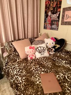 a leopard print bed spread with hello kitty pillows and stuffed animals sitting on top of it