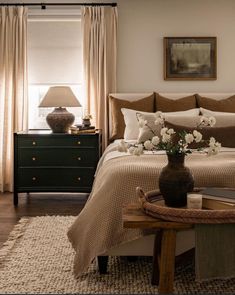 a bedroom with a bed, nightstands and flowers in a vase on the end table