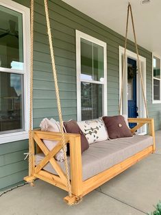 a wooden porch swing with pillows on the front and side of it, in front of a house