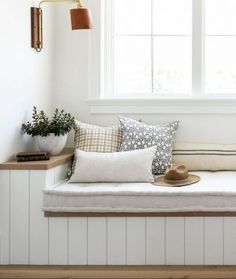 a window seat with pillows and hats on it in front of a white painted wall