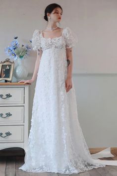 a woman in a white dress standing next to a dresser