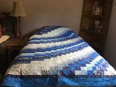 a bed with a blue quilt on top of it next to a night stand and lamp