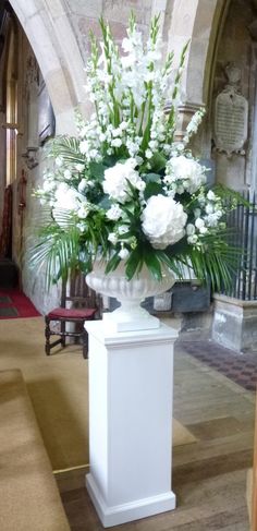 white flowers are in a large vase on a pedestal at the end of a hall