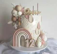 a white cake with pink and gold decorations on it's side, next to a rainbow