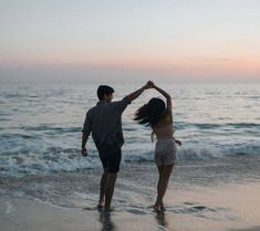 a man and woman dancing on the beach at sunset with waves crashing in front of them