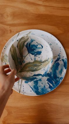 a person is holding a plate with blue flowers on it and another hand is reaching for the plate