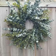 a wreath hanging on the side of a wooden fence with green leaves and foliage around it