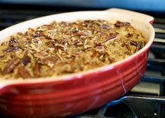 a red casserole dish filled with oatmeal and pecans in front of an oven