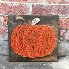 an orange string art pumpkin on a wooden block with a white lace decoration hanging from it's side