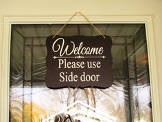 a welcome sign hanging from the side of a glass door that reads, welcome please use side door