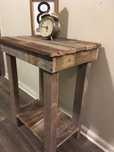 a clock sitting on top of a wooden table in front of a wall with a frame